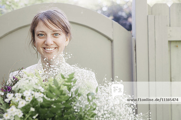 Porträt einer lächelnden Frau  die einen weißen Blumenstrauß trägt.