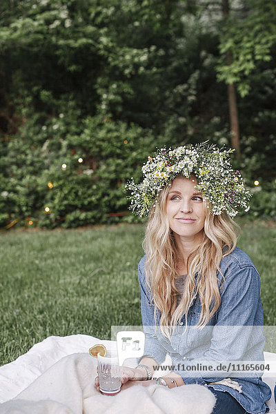 Smiling woman with a flower wreath in her hair sitting in a garden.