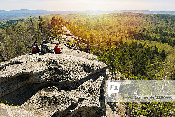 Kaukasische Freunde sitzen auf einem Bergfelsen und bewundern die malerische Aussicht