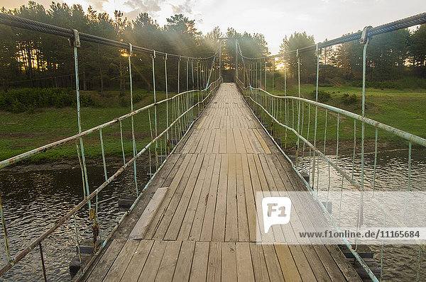 Sunbeams on wooden footbridge over river