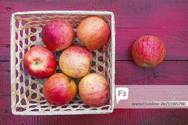 Nahaufnahme eines Korbs mit roten Äpfeln auf einem roten Holztisch