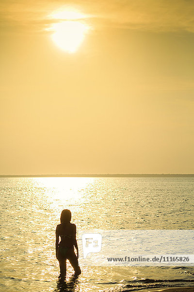 Silhouette einer gemischtrassigen Frau  die bei Sonnenuntergang im Meer watet