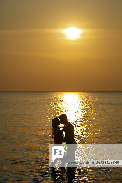 Silhouette eines kaukasischen Paares  das sich bei Sonnenuntergang im Meer küsst