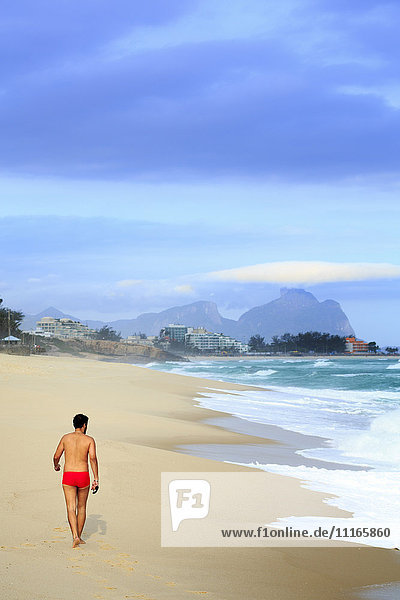Hispanischer Mann geht am Strand in der Nähe von Wellen