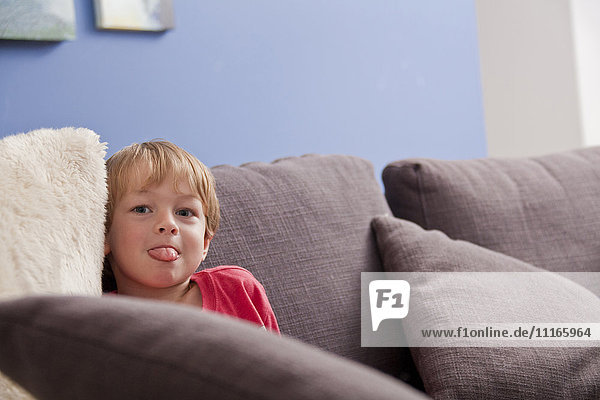 Kaukasischer Junge mit herausgestreckter Zunge auf dem Sofa