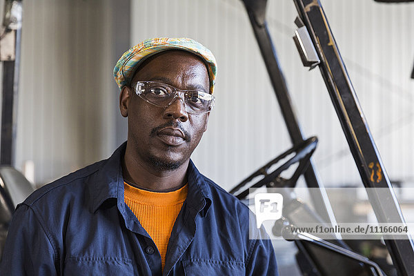 Serious Black worker posing near forklift in factory