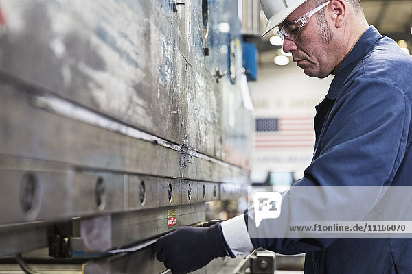 Hispanic worker fabricating metal in factory