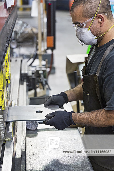 Hispanic worker wearing mask fabricating metal in factory