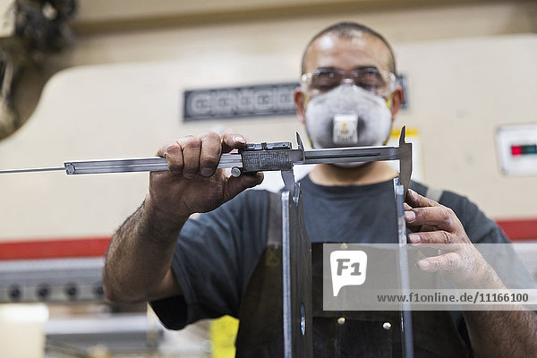 Hispanic worker measuring metal with caliper in factory