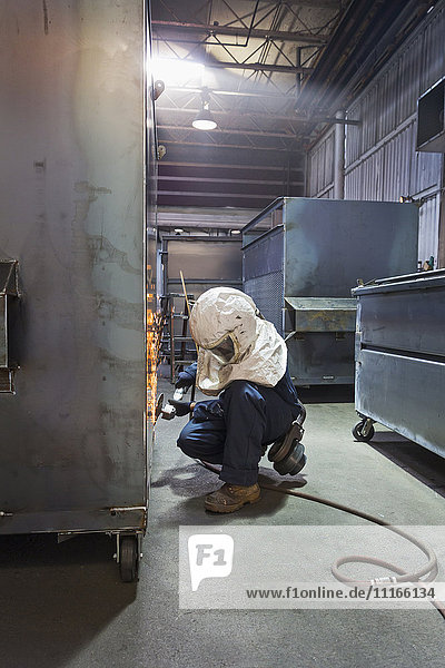 Kaukasischer Arbeiter schleift Metallbehälter in einer Fabrik