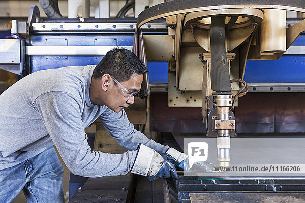 Asian worker fabricating metal in factory