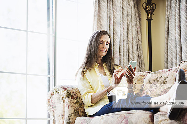 Ältere Frau mit langen braunen Haaren sitzt auf einem Sofa und benutzt ein digitales Tablett.