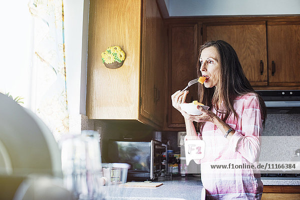 Senior woman standing in a kitchen  eating.