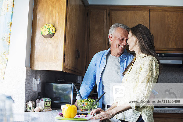 Lächelndes älteres Paar  das in einer Küche steht und Essen zubereitet.