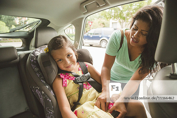 Hispanic mother buckling daughter in car seat
