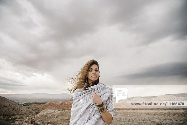 Eine Frau mit windgeblasenem Haar  eingehüllt in ein Tuch in einer Wüstenlandschaft