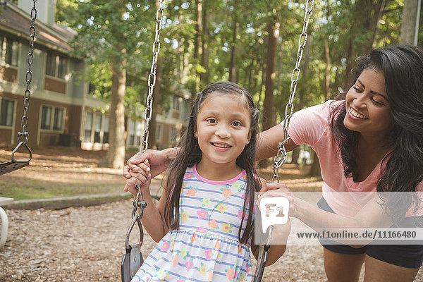 Hispanic mother pushing daughter in playground swing