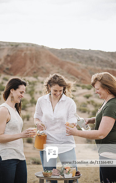Three women standing in a desert landscape having a drink.