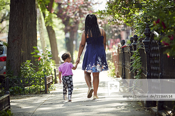 Mutter geht mit ihrer Tochter auf dem Bürgersteig spazieren