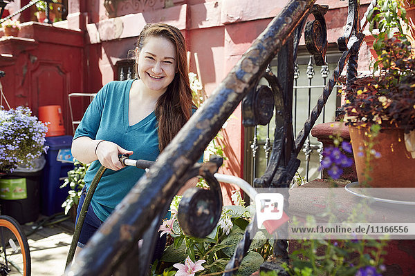 Lächelnde kaukasische Frau  die Pflanzen im Garten gießt