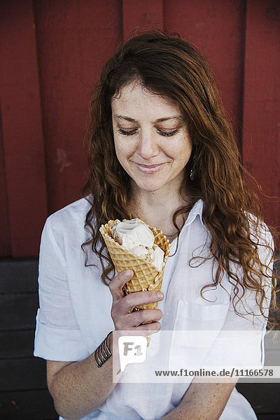 Frau mit langen braunen Haaren sitzt auf einer Bank und isst Eiscreme.