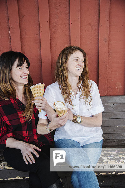 Zwei Frauen sitzen auf einer Bank und essen Eiscreme.