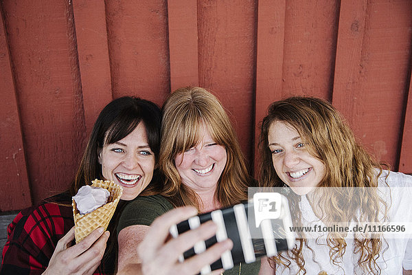 Drei Frauen essen Eiscreme und machen einen Selfie mit dem Handy.