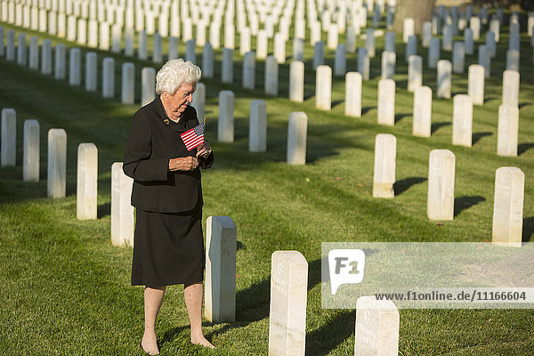 Caucasian widow holding American flag at cemetery gravestone