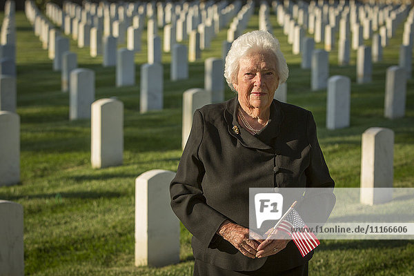 Caucasian widow holding American flag in cemetery