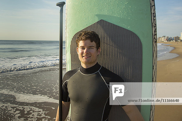 Man posing with paddleboard on beach