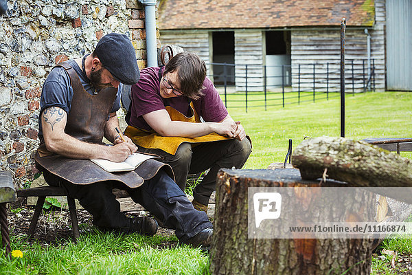 Zwei Schmiede  ein Mann und eine Frau mit Schürzen  die in ein Notizbuch schreiben  saßen in einem Garten.