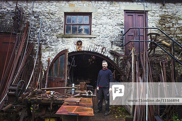 Blacksmith standing outside his workshop  looking at camera.