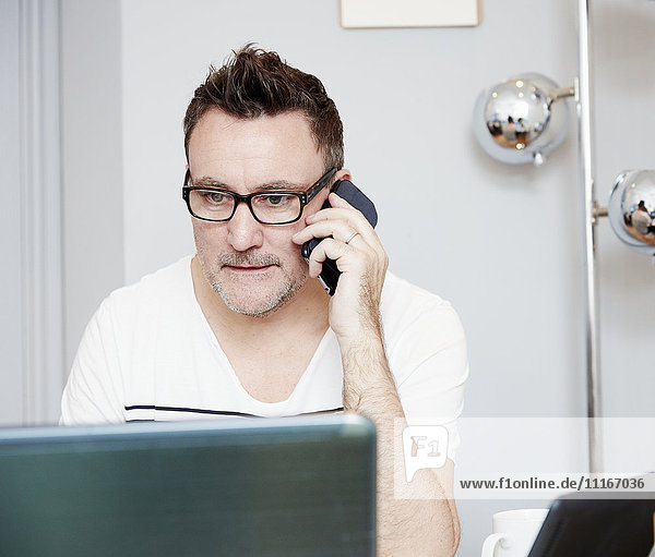 Ein Mann  der am Schreibtisch in einem Büro vor einem Laptop sitzt  am Telefon.