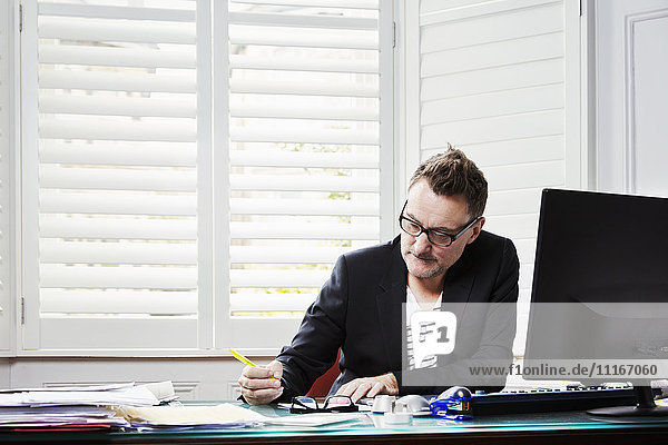 Ein Mann  der in einem Büro am Schreibtisch sitzt  arbeitet und einen Stift hält.
