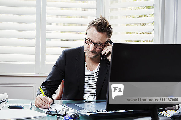 Ein Mann sitzt in einem Büro am Schreibtisch  einen Stift in der Hand  am Telefon.