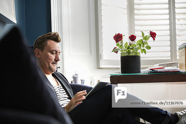 Mann sitzt in einem Büro und benutzt sein Mobiltelefon  eine Vase mit roten Rosen auf einem Schreibtisch.