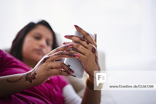 Frau mit Henna-Tattoos auf den Händen  die eine SMS auf einem Mobiltelefon schreibt