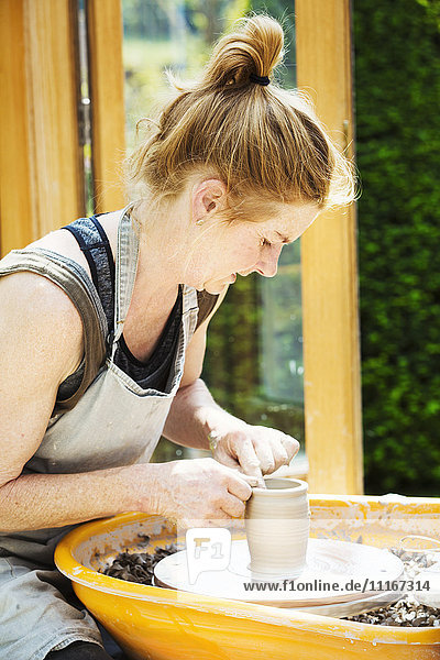 Eine Töpferin  die in ihrer Werkstatt Ton auf einer Töpferscheibe bearbeitet.