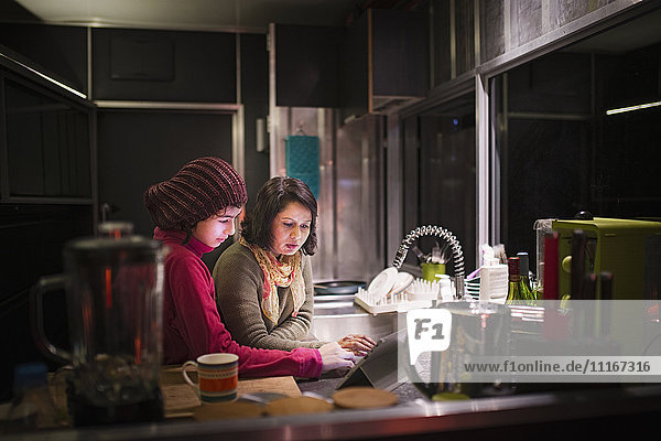 Mutter und Tochter benutzen nachts ein digitales Tablet in der Küche
