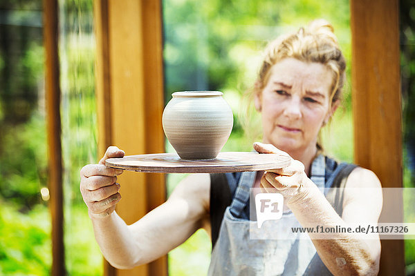 A potter examining a hand thrown pot  wet clay slip  rounded vase with tapering sides.