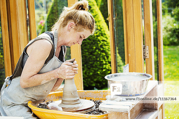 Eine Töpferin  die in ihrer Werkstatt Ton auf einer Töpferscheibe bearbeitet.