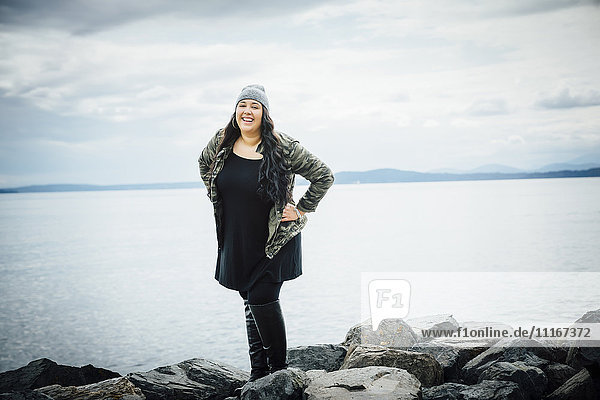 Lächelnde Mixed Race Frau posiert auf Felsen in der Nähe von Meer