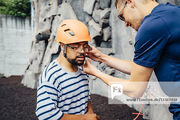 Man helping rock climber fasten helmet