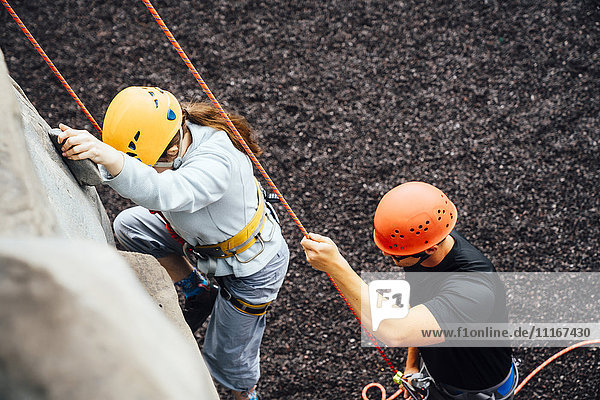 Caucasian man holding rope for woman climbing rock climbing wall