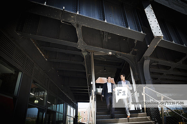 Zwei Geschäftsleute in grauen Anzügen gehen am Eingang eines Gebäudes eine Treppe hinunter.