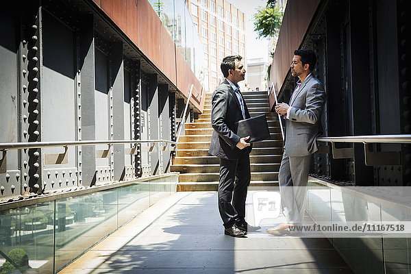 Zwei Geschäftsleute in grauen Anzügen stehen im Freien und unterhalten sich miteinander.
