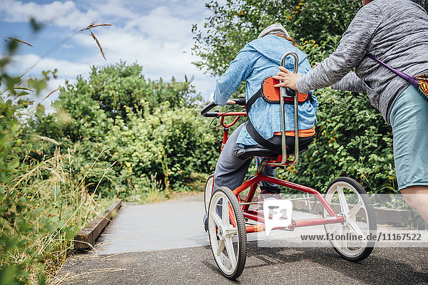 Caucasian woman pushing daughter riding tricycle