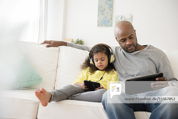 Vater und Tochter benutzen digitale Tablets auf dem Sofa