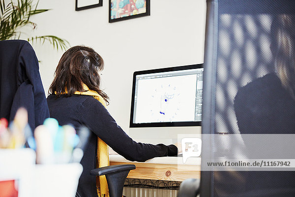 Eine Frau  die an einem Computerbildschirm an einem Schreibtisch in einem Büro arbeitet. Rückansicht.