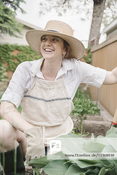 Eine Frau mit einem Strohhut mit breiter Krempe  die in einem Garten arbeitet und gräbt.